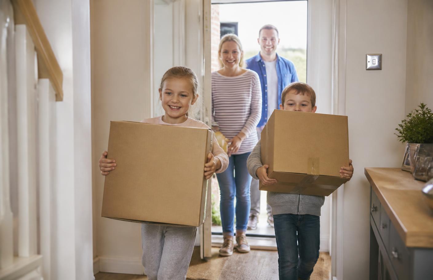 A British family carrying moving boxes into the hallway of their new home